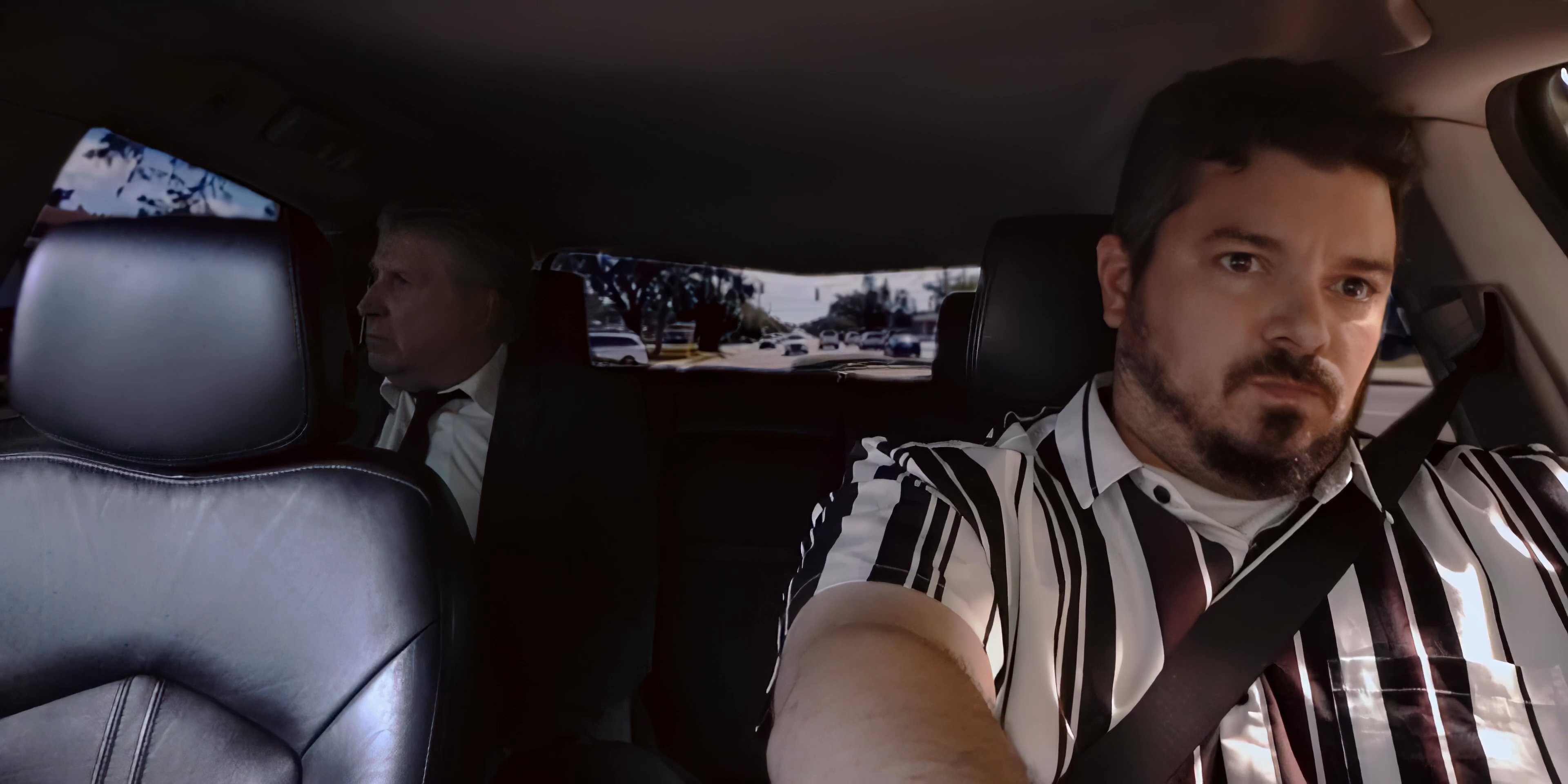 Two men travel together in a car while conversing, followed by a transition to an expansive aerial view of an urban landscape.