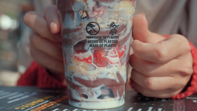 A girl turning a plastic cup filled with chocolate ice cream