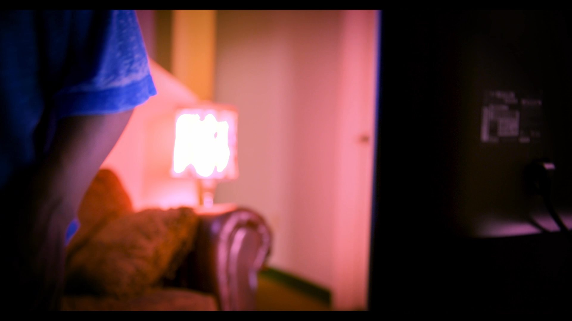 A man watches a video on a television in a dimly lit room, contemplating memories while navigating a sense of loss and isolation.