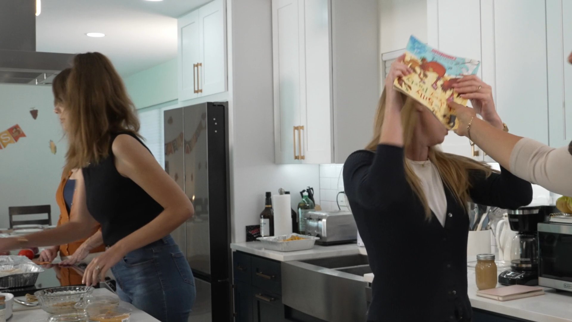 A diverse group of adults and a teenager interact within a modern residential kitchen during a social gathering.