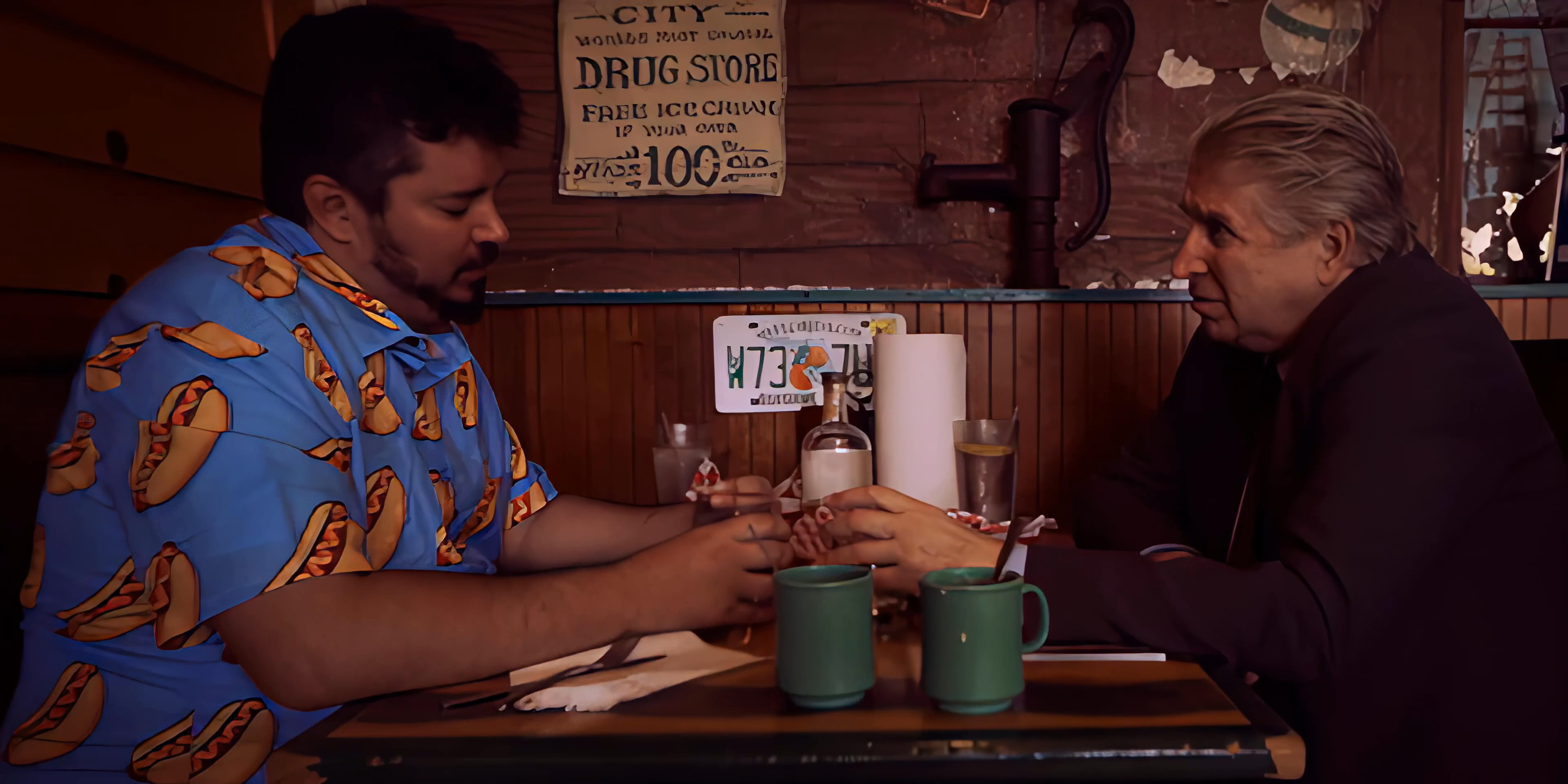 Two men engage in a focused discussion while seated across from each other in a booth at a retro-style diner.