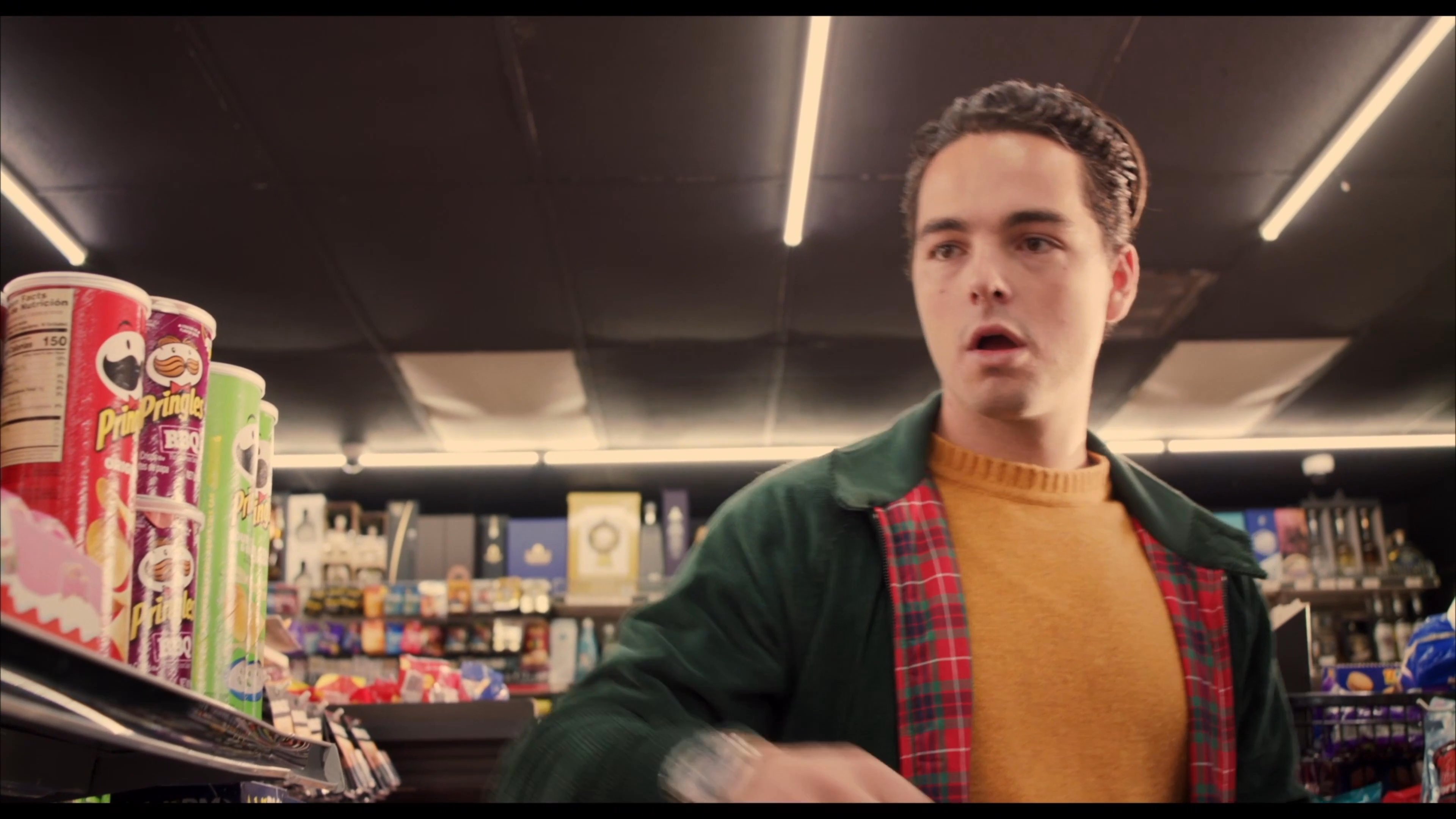 A man carefully inspects items on store shelves while browsing the aisles of a convenience store. He examines specific products before continuing his shopping trip in the retail setting.