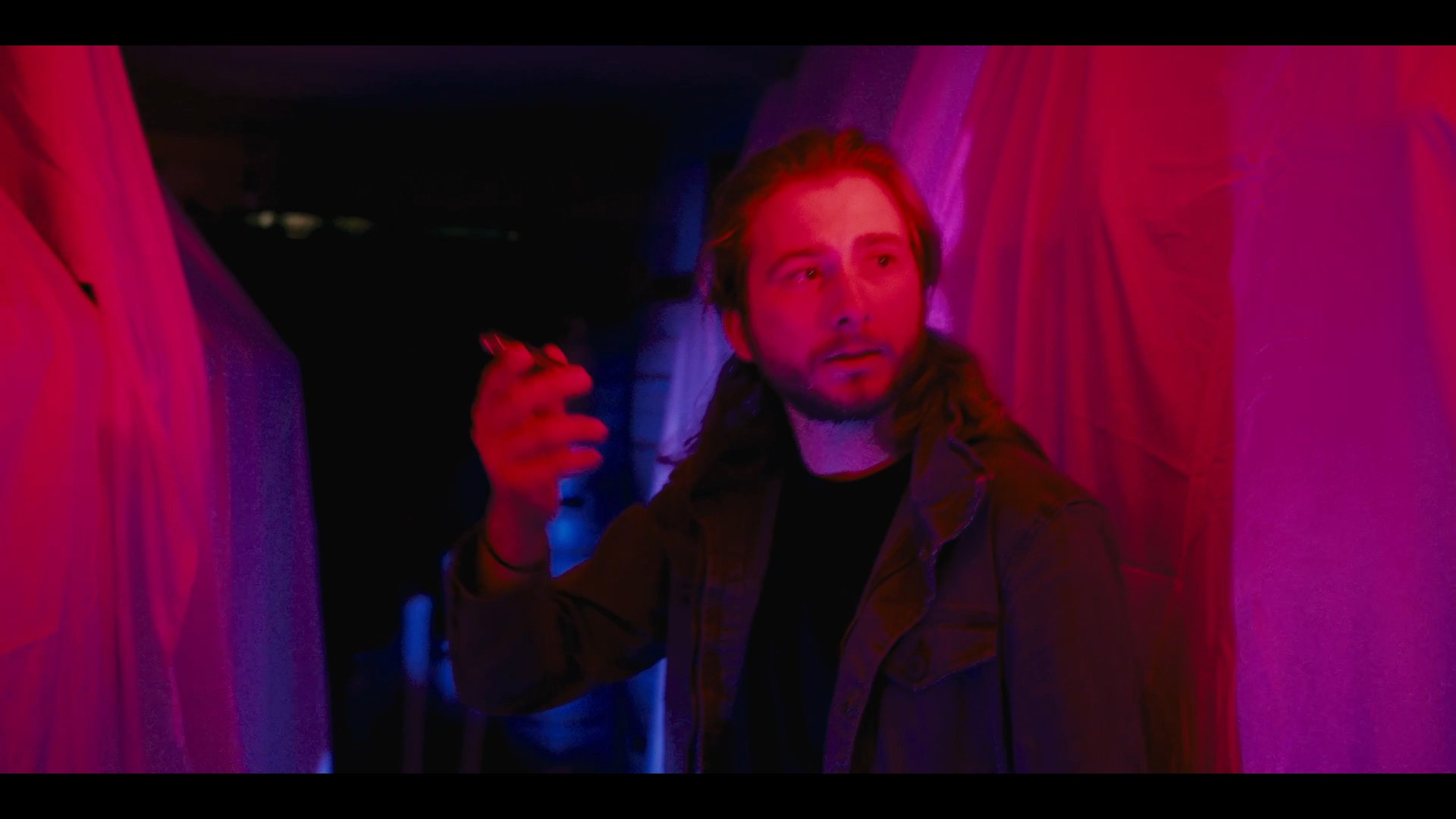 A man observes light and color shifts in an atmospheric, draped environment before transitioning to a woman operating professional equipment in a workshop setting.