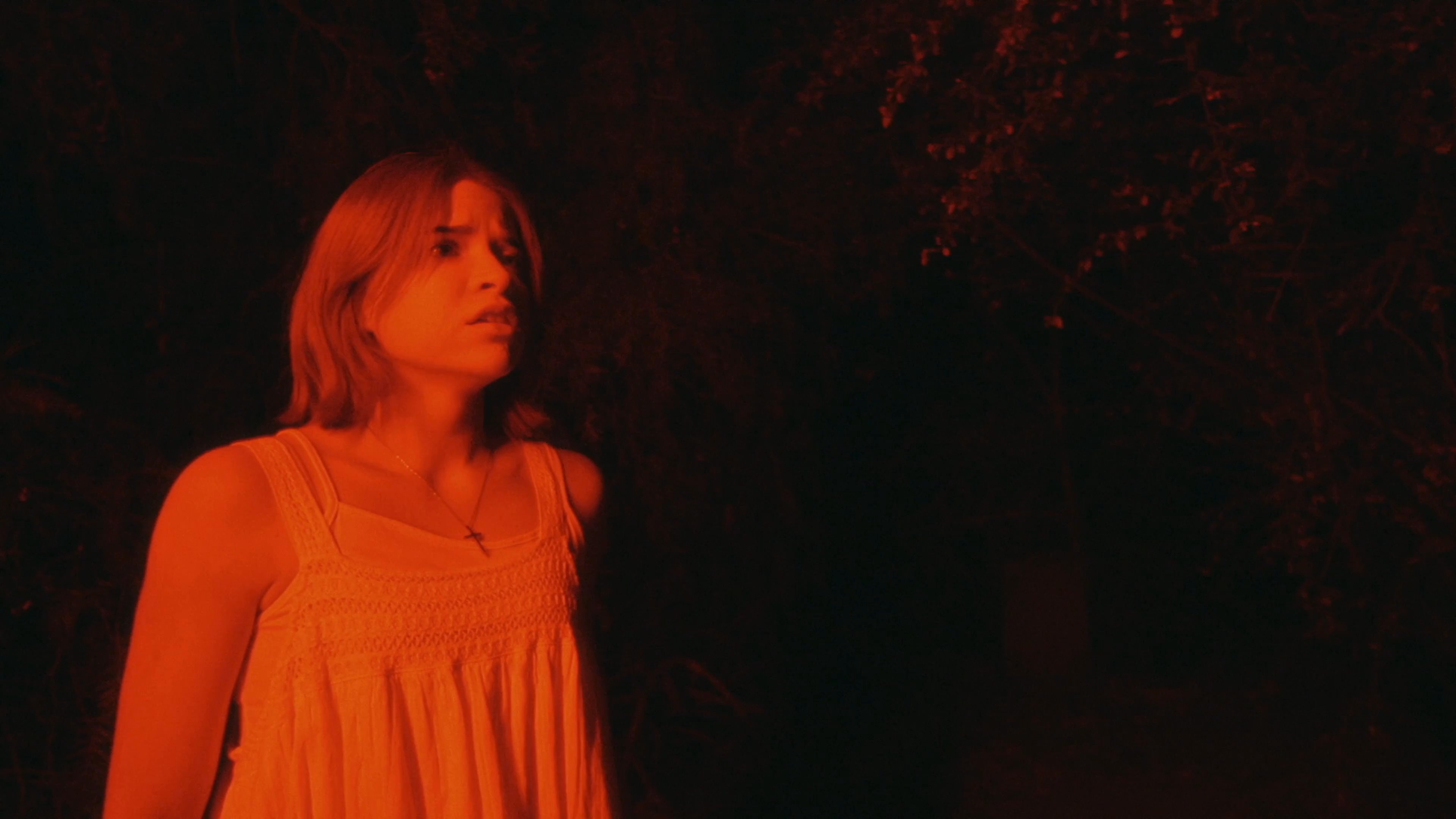 A woman in a white nightgown flees through a dark, red-lit environment while experiencing a disorienting, supernatural encounter. Her facial expressions convey growing panic and distress as she attempts to escape an unseen threat.