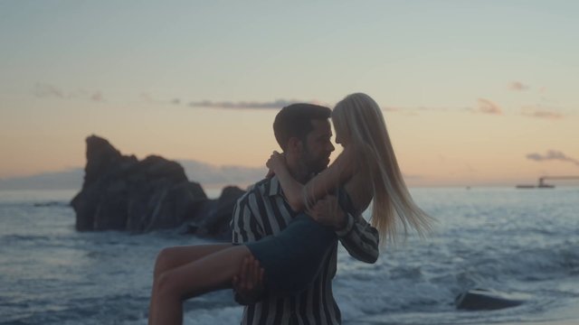 A man picking up a woman with his arms at the beach