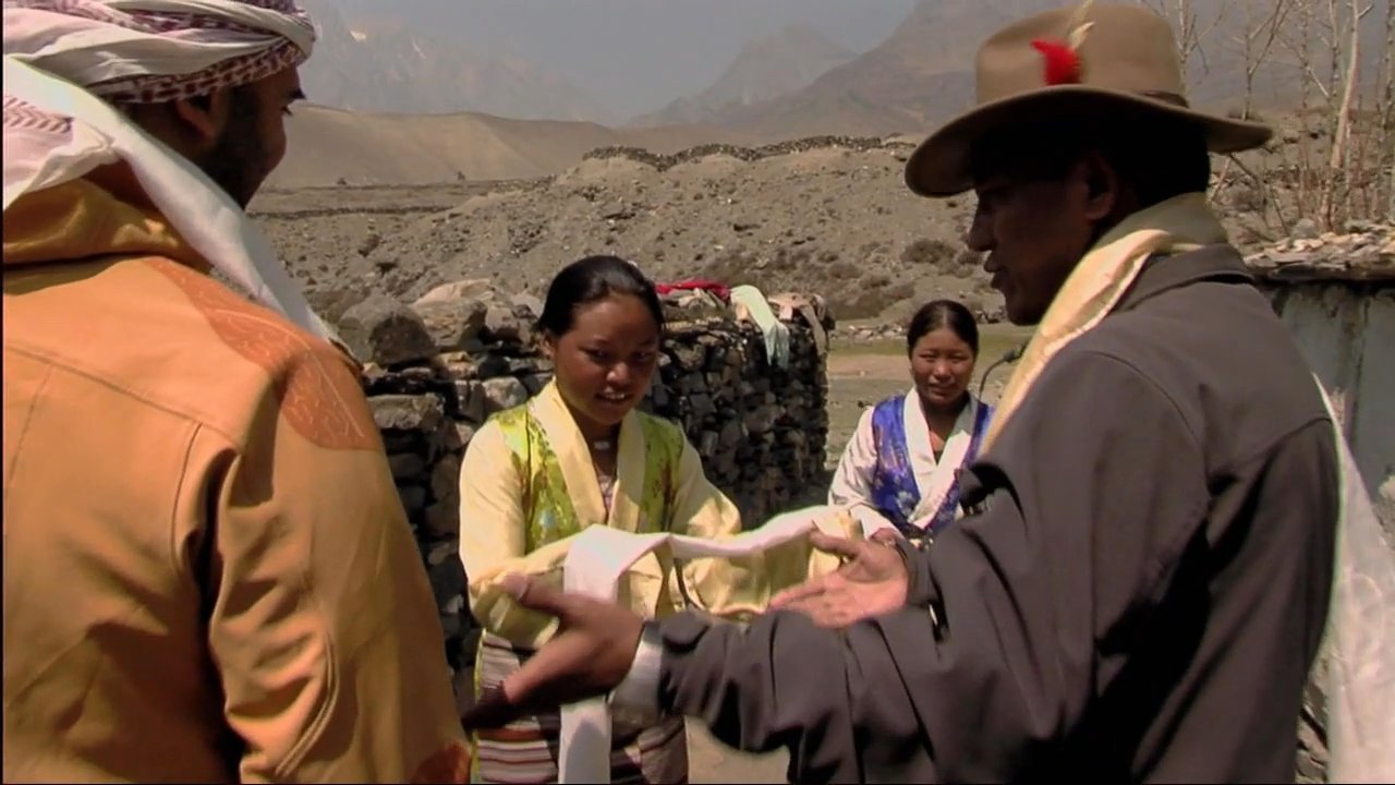 Visitors arrive on horseback at the Dakmar Day Care Center and are greeted by locals with traditional ceremonial scarves. The group enters the facility to engage with the community and children gathered at the entrance.