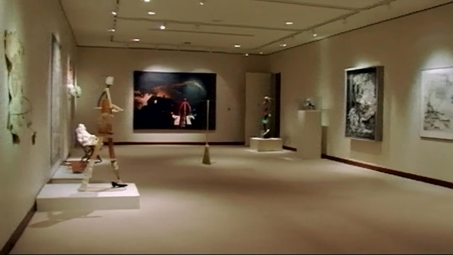 An elderly man in a green cap and a woman in a bright magenta jacket walk through a gallery, viewing colorful paintings and sculptures. They discuss the artworks, and he warmly praises one piece as they continue through the exhibition.