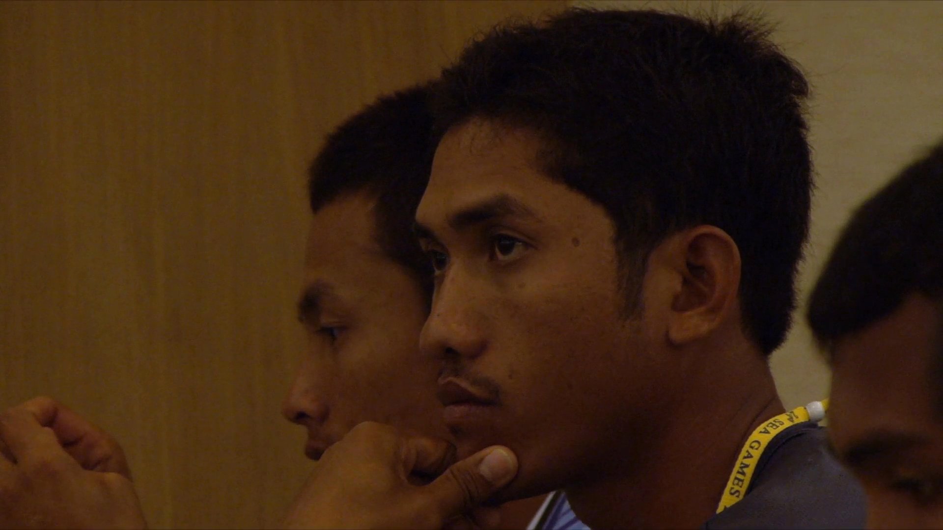 Athletes in team uniforms attend a formal briefing in a conference setting, with a representative speaker leading the discussion while other team members listen attentively.