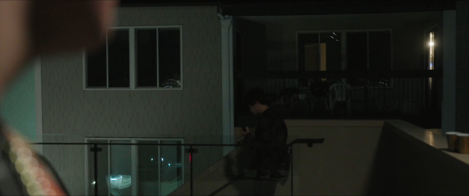 A young man steps away from a group social gathering at night to take a serious phone call inside a quiet room.