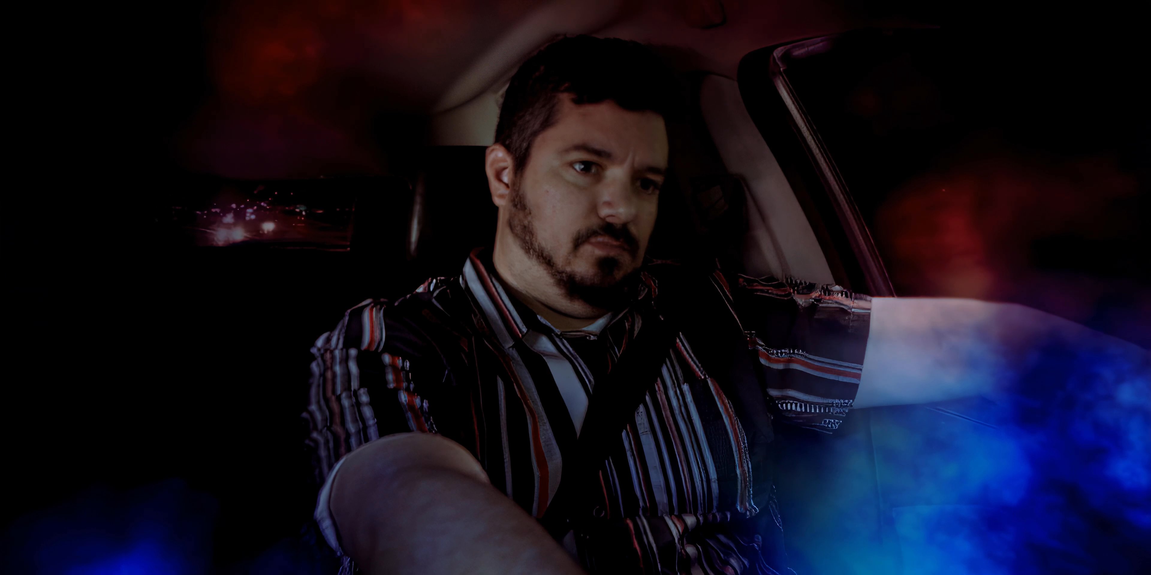 A man drives along a highway at night, surrounded by ethereal, colorful mist that blends with the passing city lights. The scene captures a meditative and dreamlike transit experience.