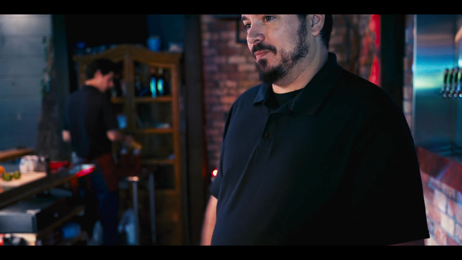 A bartender works behind a bar, preparing ingredients and organizing the workspace in a dimly lit, professional restaurant setting.