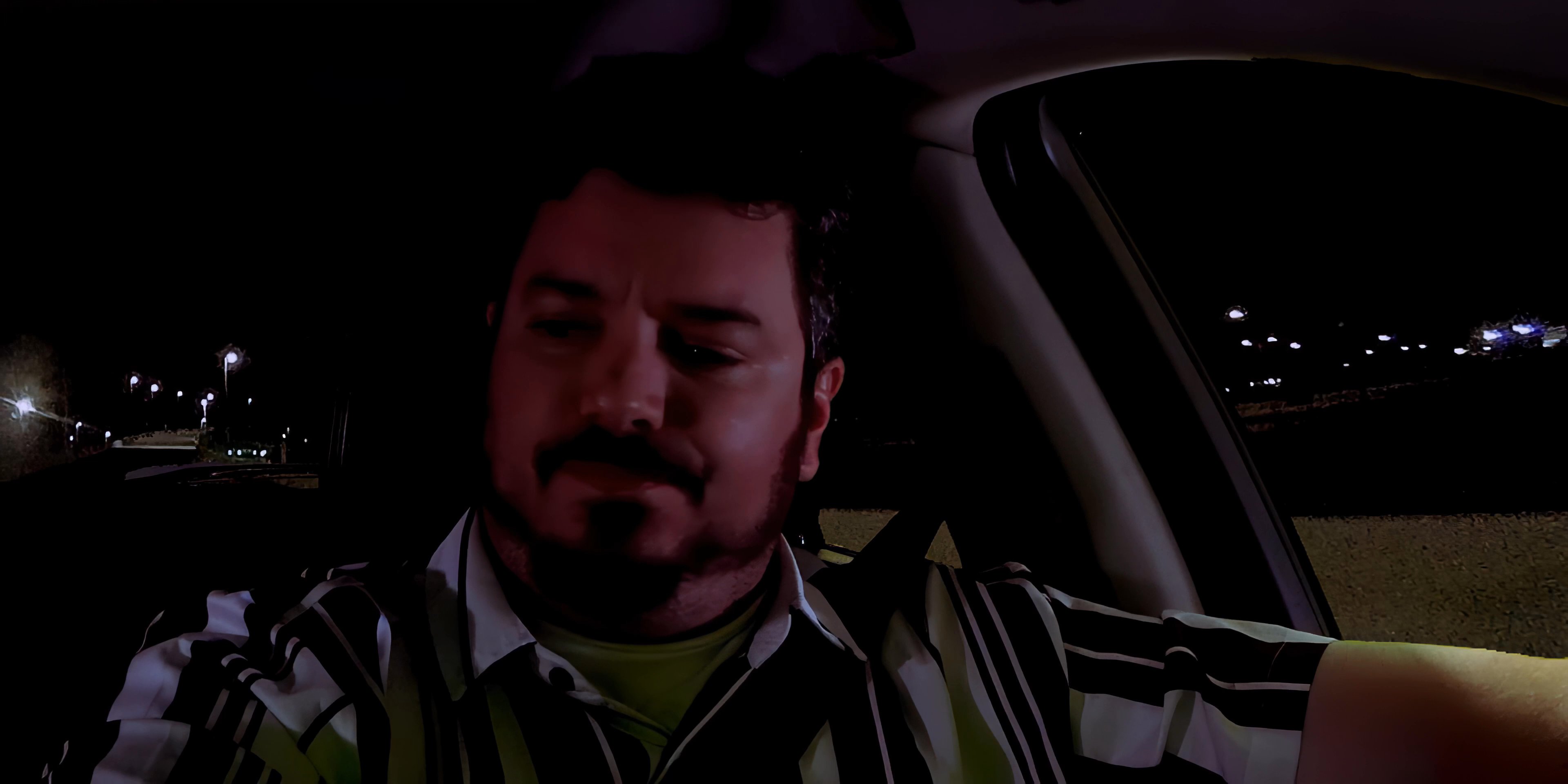 A man drives at night while engaged in a conversation on his vehicle-mounted smartphone. The scene captures his focused expression as he navigates in the dark.
