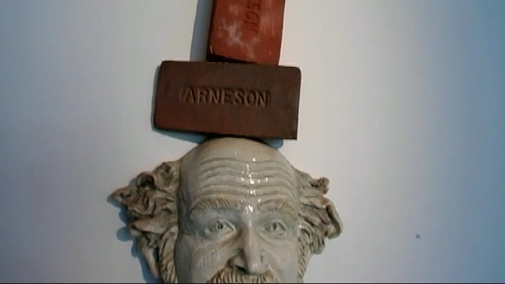 A man discusses Renee and his colorful, provocative collection in a garden interview. The collection includes a grotesque wall-mounted assemblage and an elaborately customized vintage car.