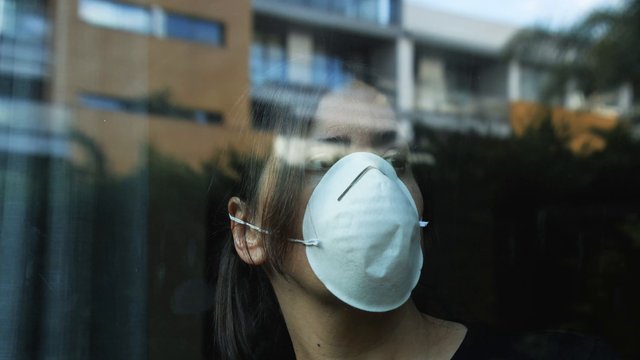 Masked woman looking out window