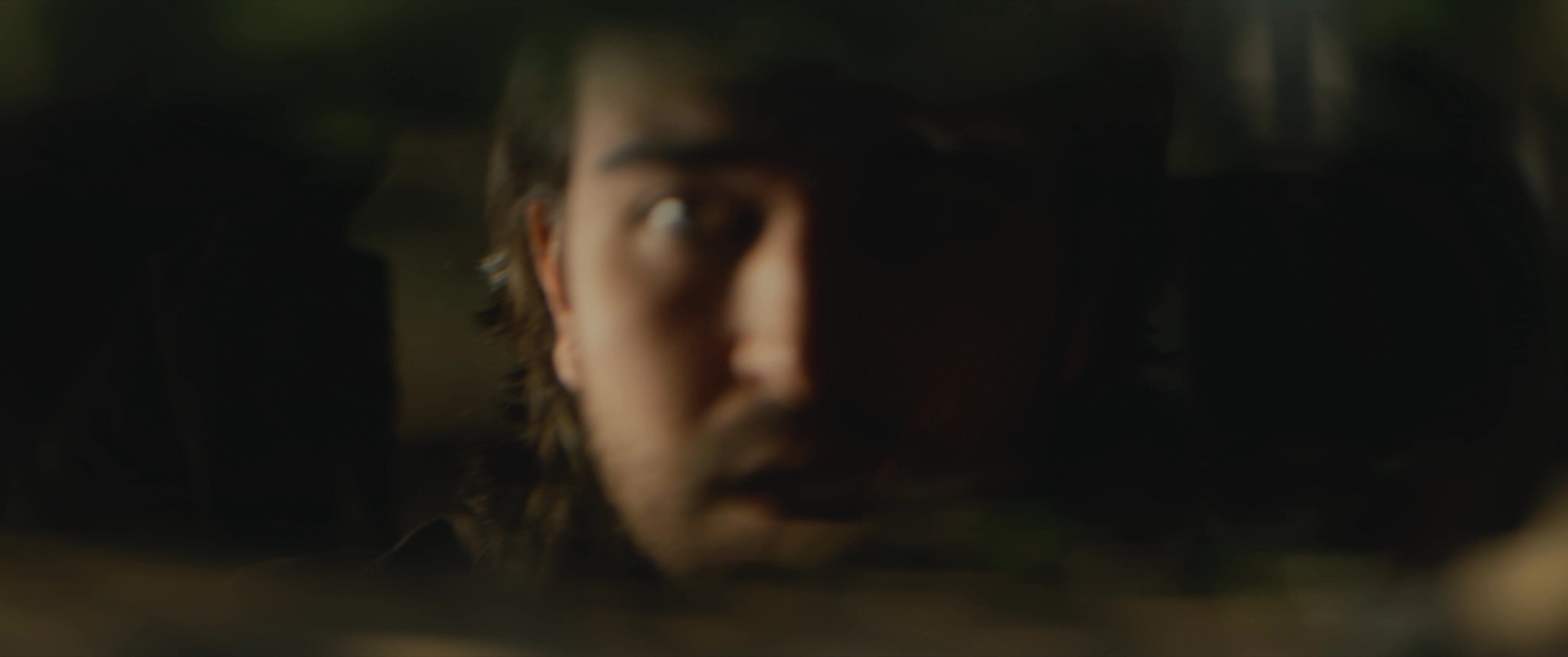 A man exhibits signs of deep fatigue while seated in his vehicle before focusing intently on his reflection, which shifts in appearance. The scene captures a tense, atmospheric moment of internal or supernatural transition.