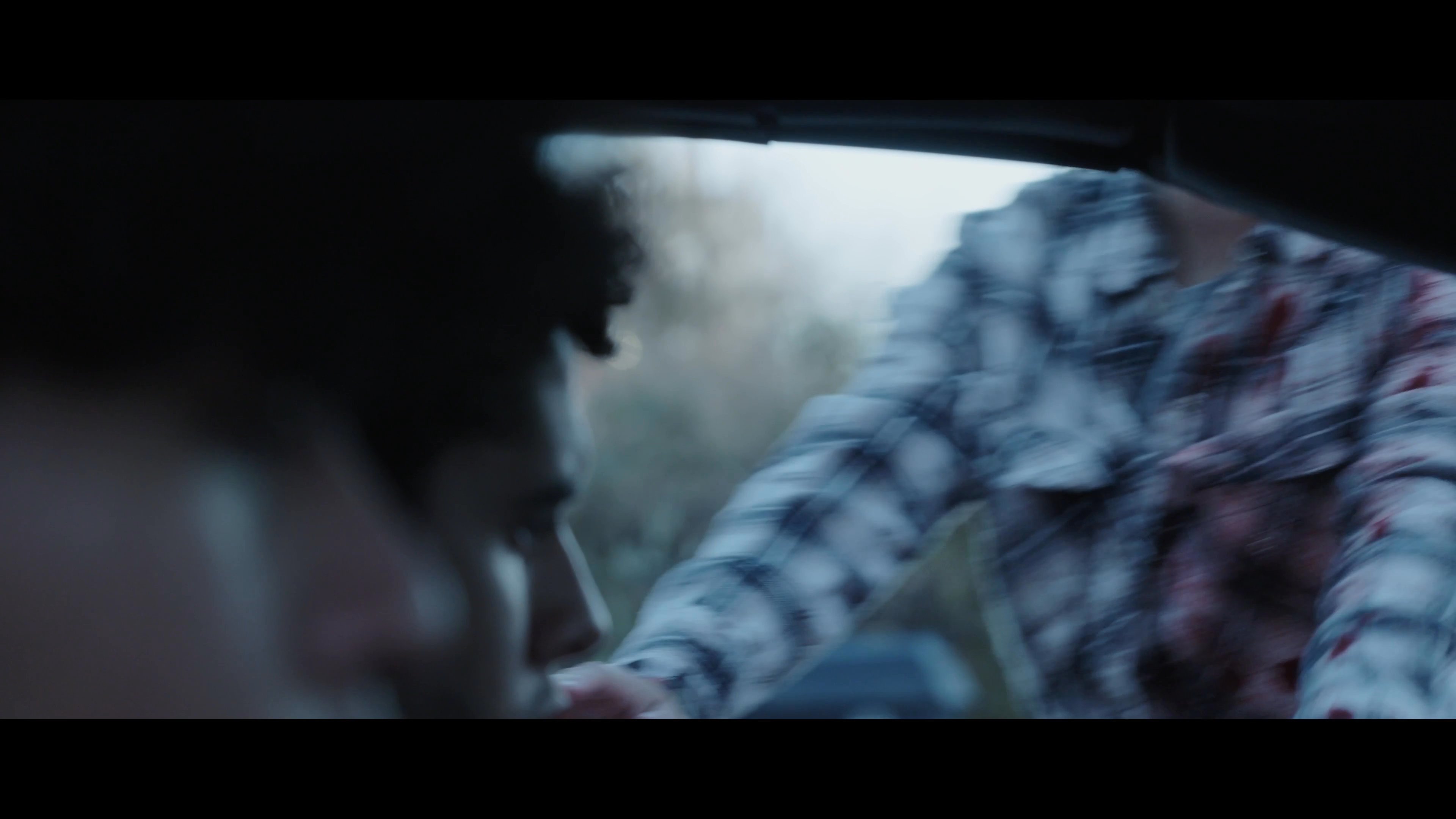 An injured woman covered in blood approaches a vehicle on a residential street to confront the occupants. The interaction develops with visible tension as she engages the driver.