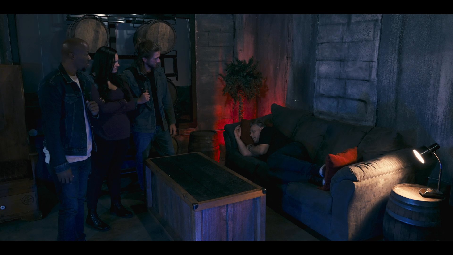 A group of individuals convenes in a dimly lit, industrial-style safehouse to discuss sensitive objectives. The atmosphere is tense as they coordinate their next move in a secured, secluded space.