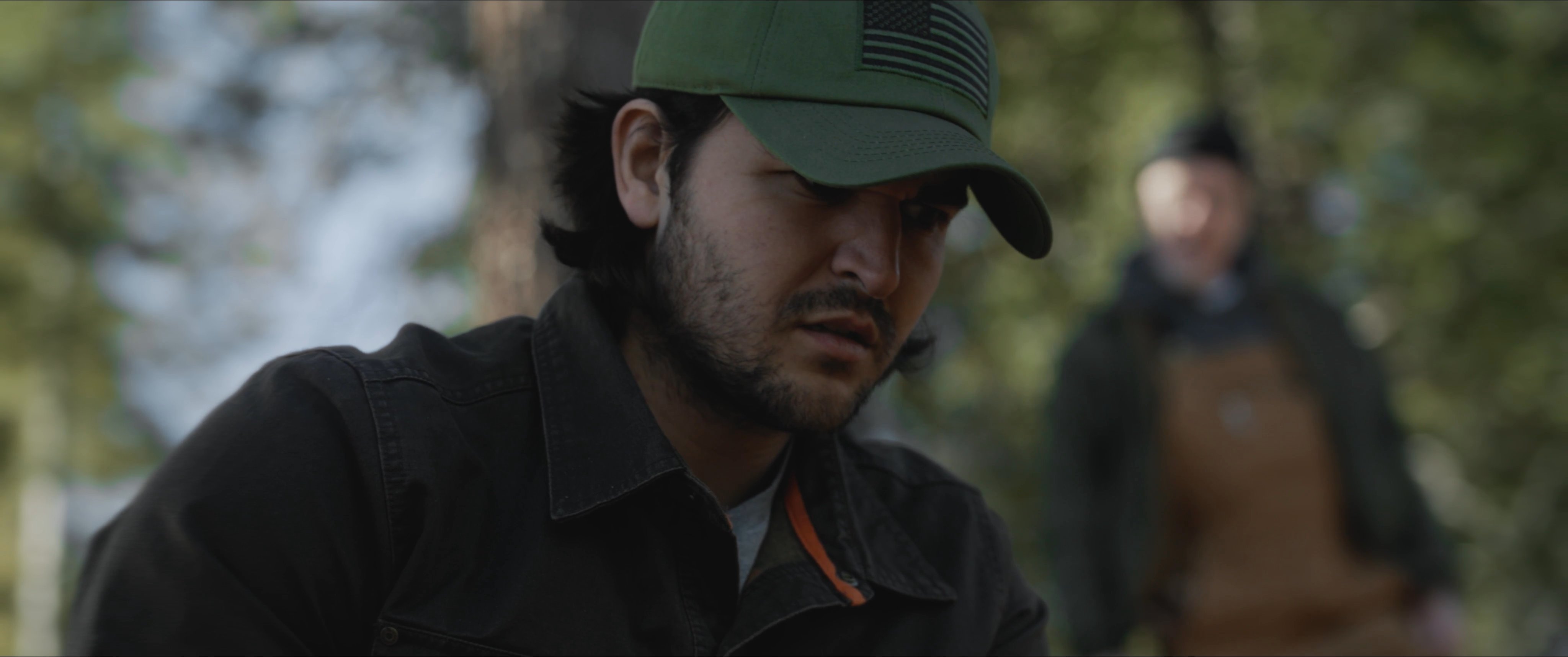 Two individuals conduct a survey in a wooded area, focusing on a small, hand-held artifact retrieved from the soil. The interaction suggests a moment of significance during an active excavation project.