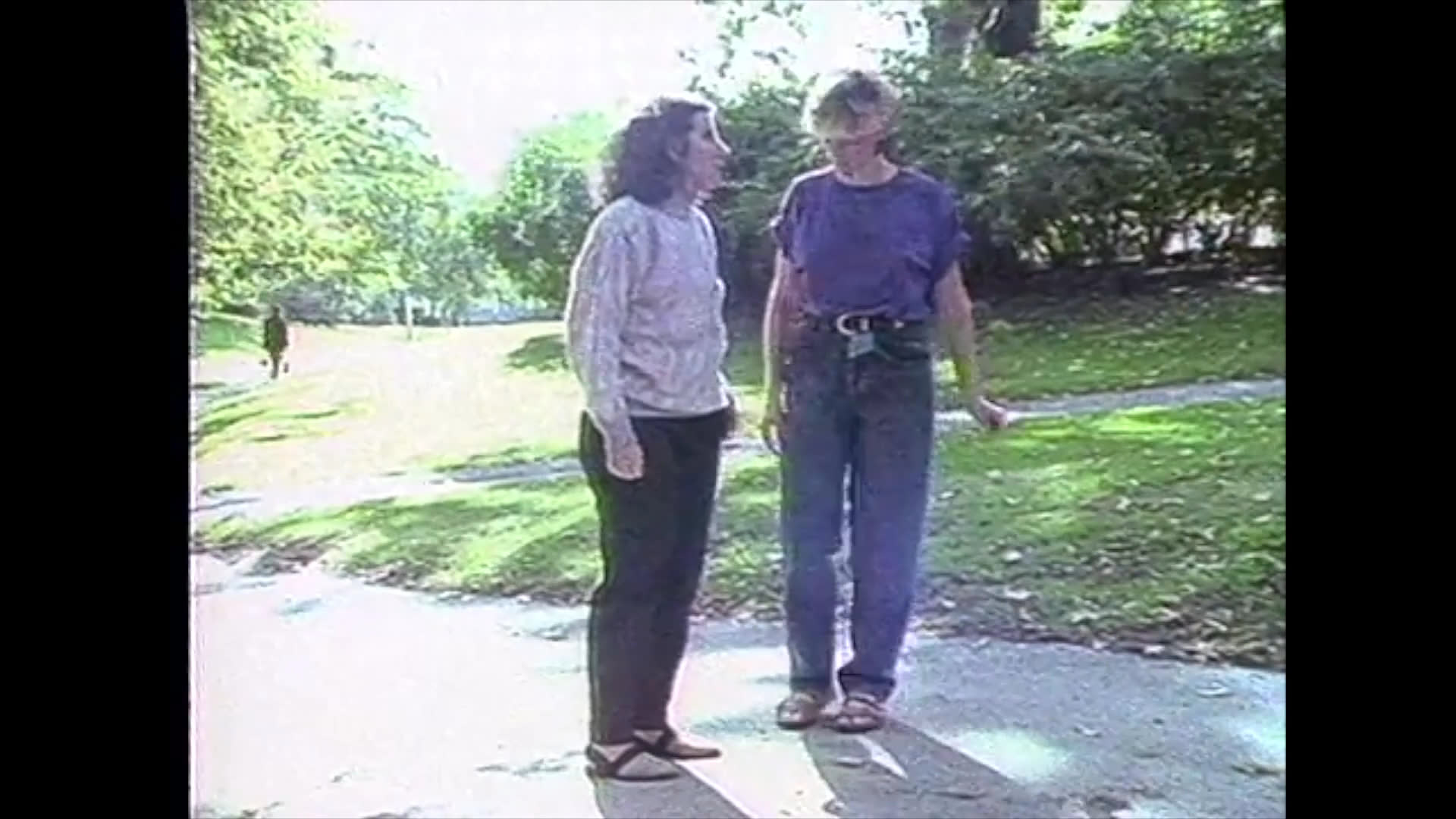 A man speaks in a formal setting before the scene transitions to two women engaging in conversation and walking through a public park area.