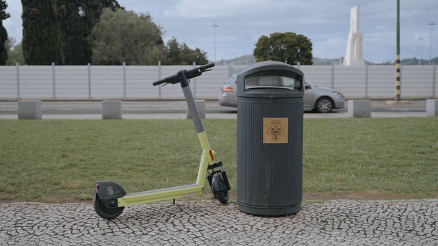 Un scooter eléctrico está estacionado cerca de un cubo de basura.