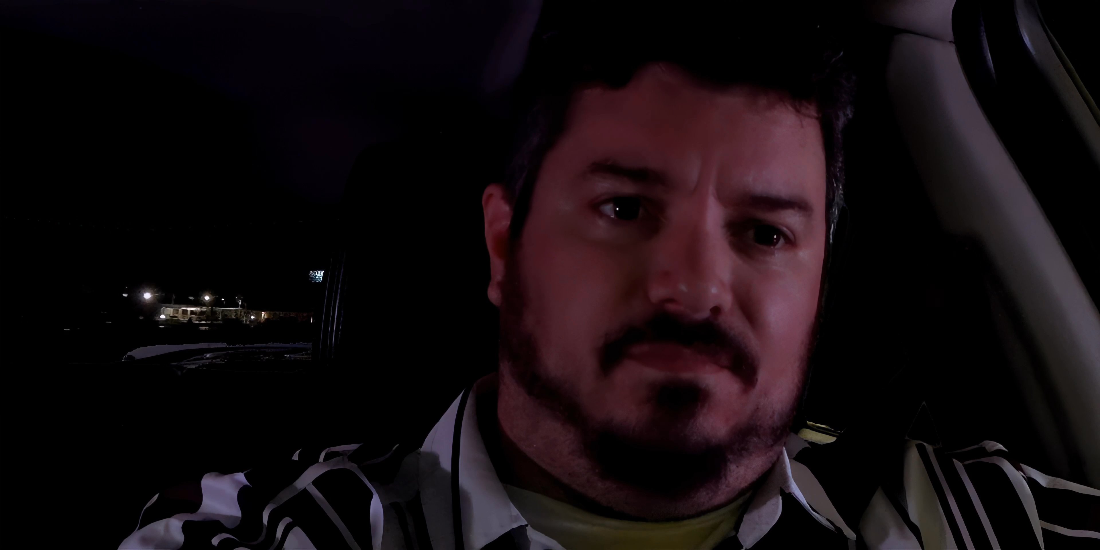 A man sits in the driver's seat of a car at night while engaged in a hands-free phone conversation, maintaining focus on the road ahead.