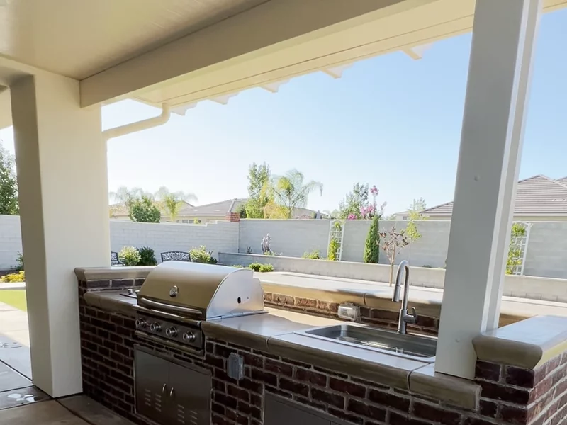 Brick outdoor kitchen  with built in sink, grill, and storage under a white parabola