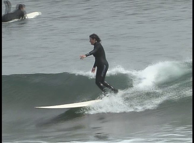 A surfer shares insights during an interview before demonstrating wave-riding techniques on the ocean. The sequence alternates between close-up commentary and active long-shots of the individual riding various waves.