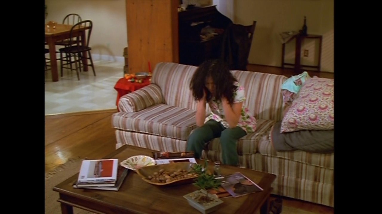 A man and woman experience a moment of emotional tension in a living room before the man transitions to practicing his golf putting on a mat in a dark, spacious room.