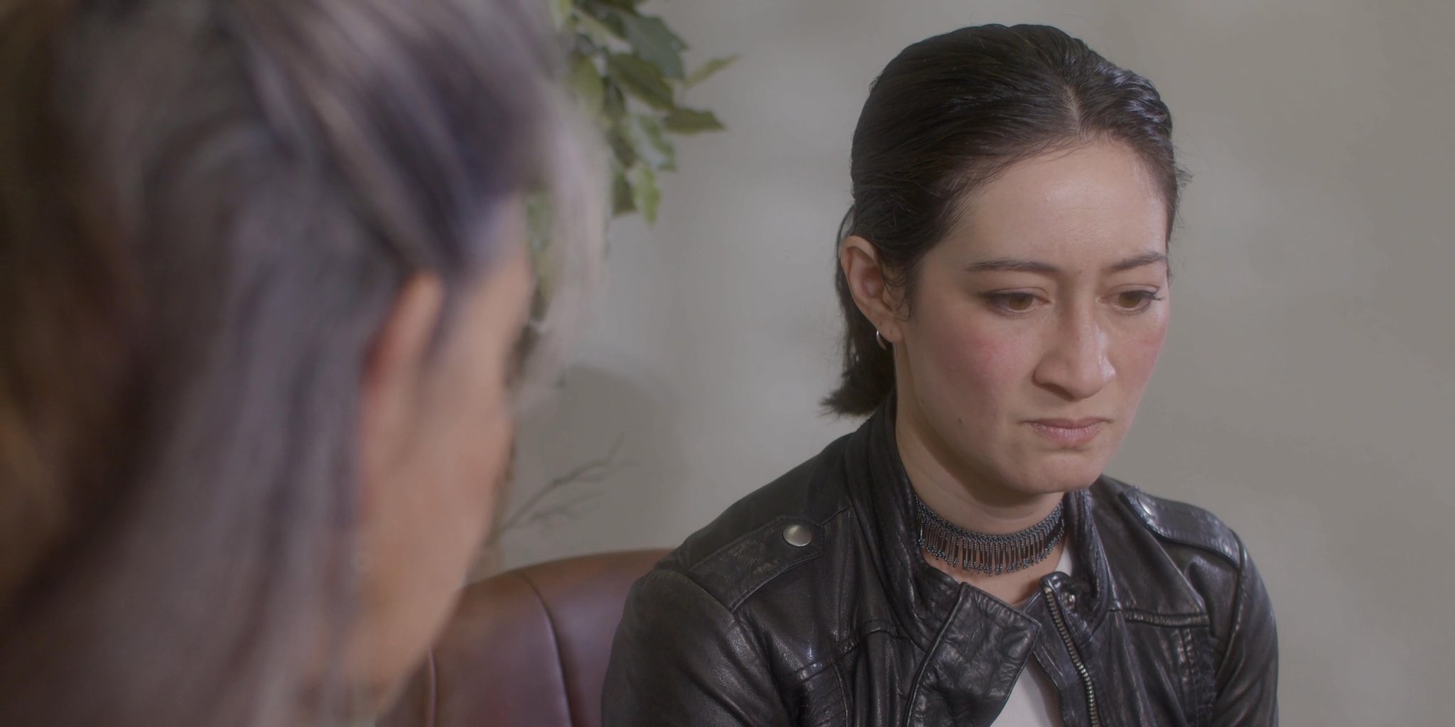 Two women engage in a focused, serious conversation while seated in a home setting. The exchange emphasizes active listening and mutual engagement between a mentor and a client.