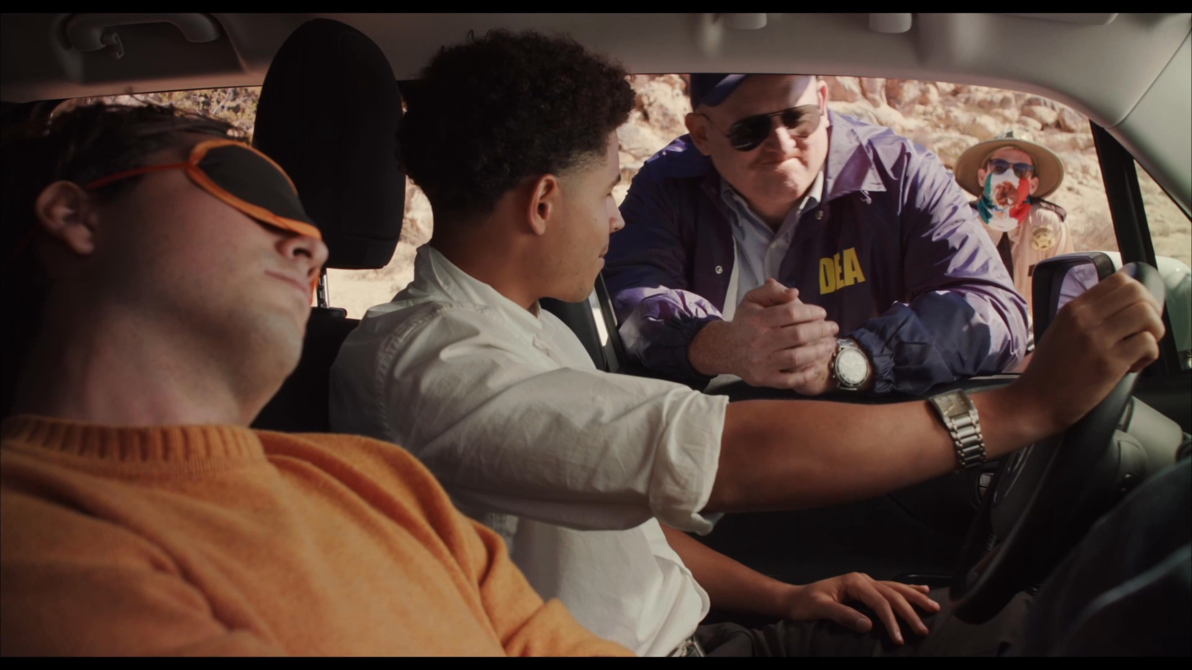 A DEA agent conducts a field interview with occupants inside a vehicle stopped at a desert checkpoint.