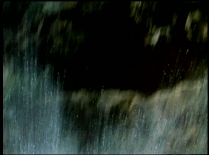 A woman narrates personal recollections while footage captures individuals diving from rocky cliffs into a natural waterfall basin. The scenes contrast lush tropical surroundings with the athletic activity of swimmers entering the water.