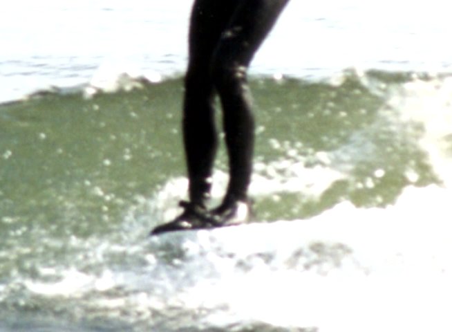 Athletes in wetsuits navigate waves on surfboards in an open ocean environment, demonstrating balance and surfing technique.