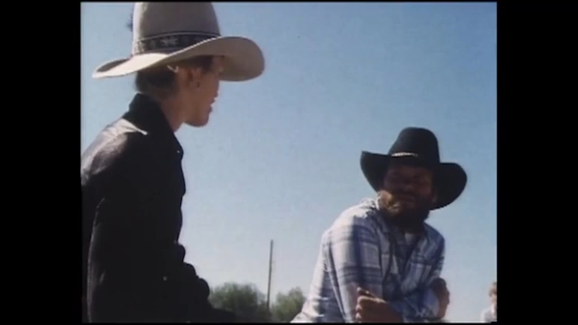 Riders cross a dusty outdoor arena before an adult helps a young rider on a saddled horse. The activity centers on welcoming local children, enjoying the sport, and learning good sportsmanship over winning.