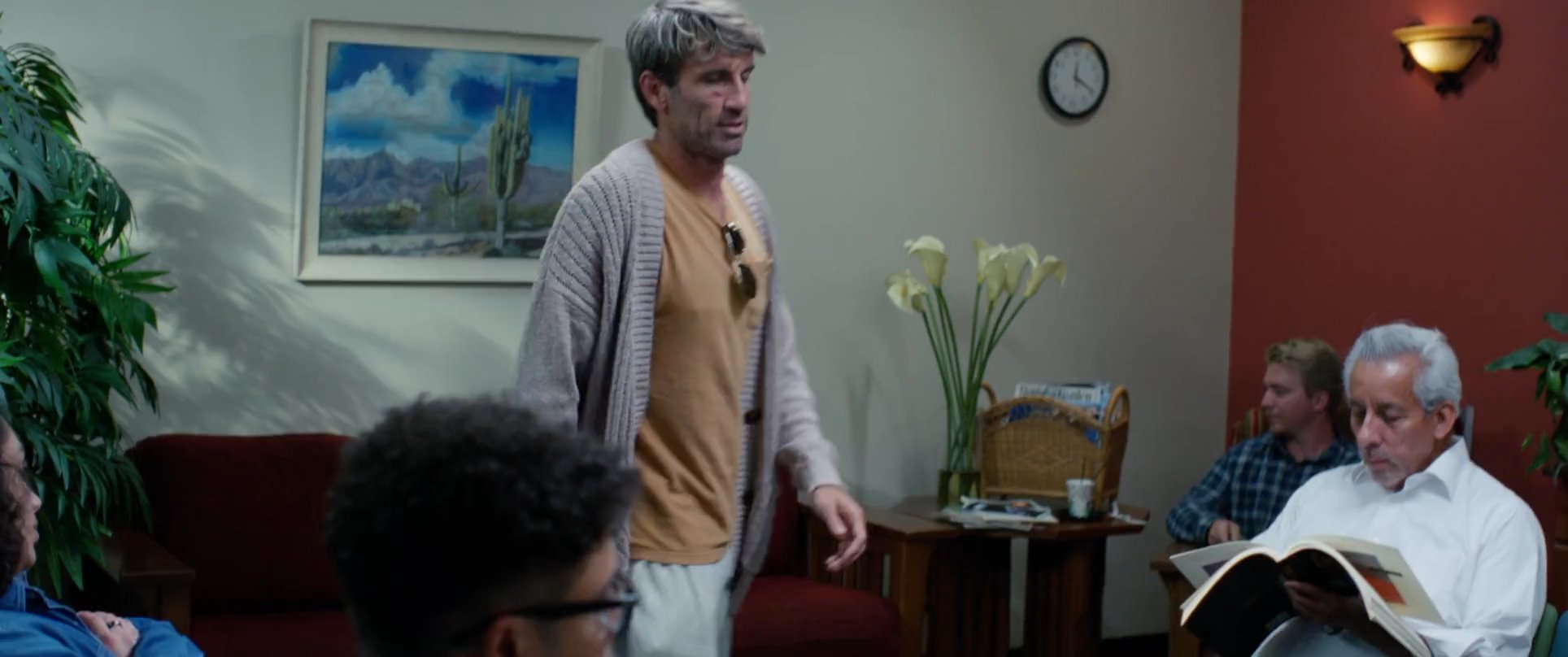 A man arrives at a medical or office facility in a vintage truck and walks into a quiet waiting room to check in at the reception desk.