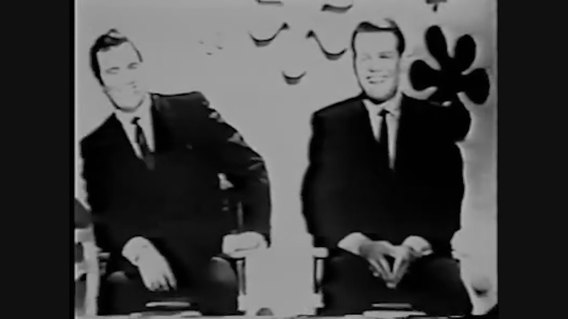 Panelists participate in a classic game show, featuring a conversation moderated by the voice of Chuck Barris within a stylized, decorative studio set.