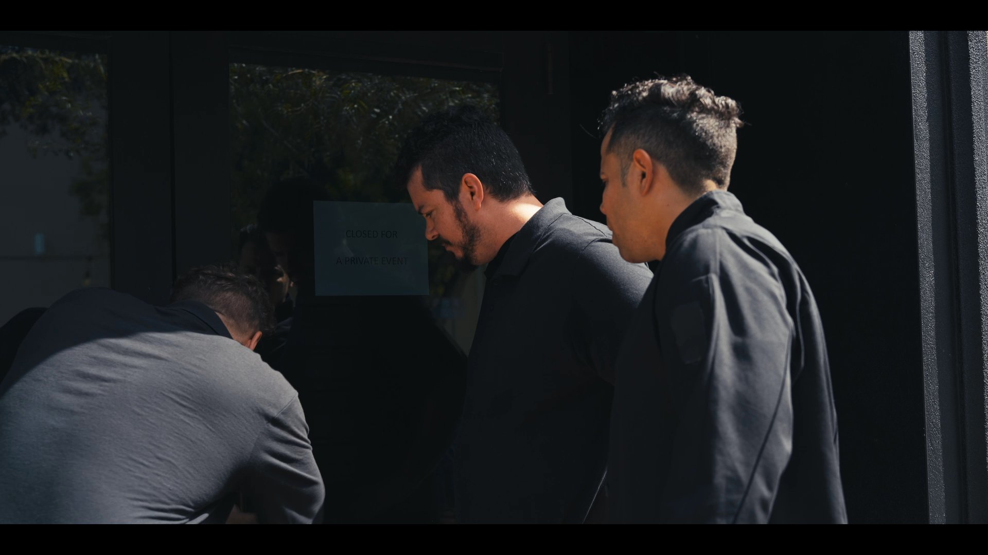 Three individuals coordinate at an entrance before entering a sophisticated, modern office space together. Their interaction suggests a professional meeting or collaborative effort.