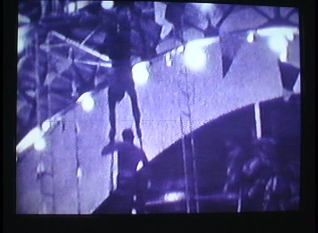 Performers execute a coordinated acrobatic routine on a high-level apparatus in front of a live audience. The sequence highlights precise physical maneuvers and strength-based feats during a circus exhibition.