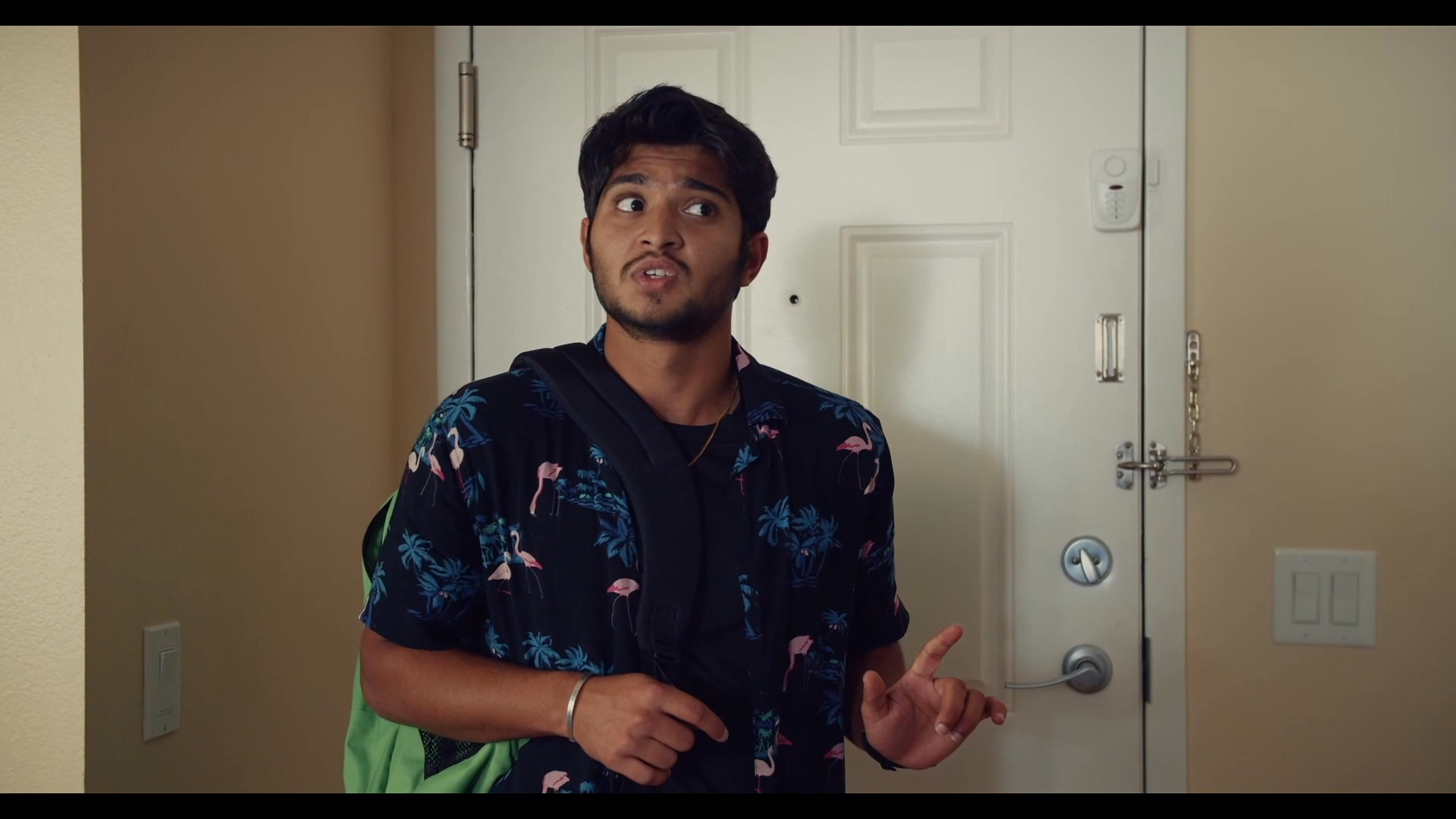 Two young men engage in a discussion inside an apartment living space. The interaction involves verbal exchange and mutual observation within their shared environment.