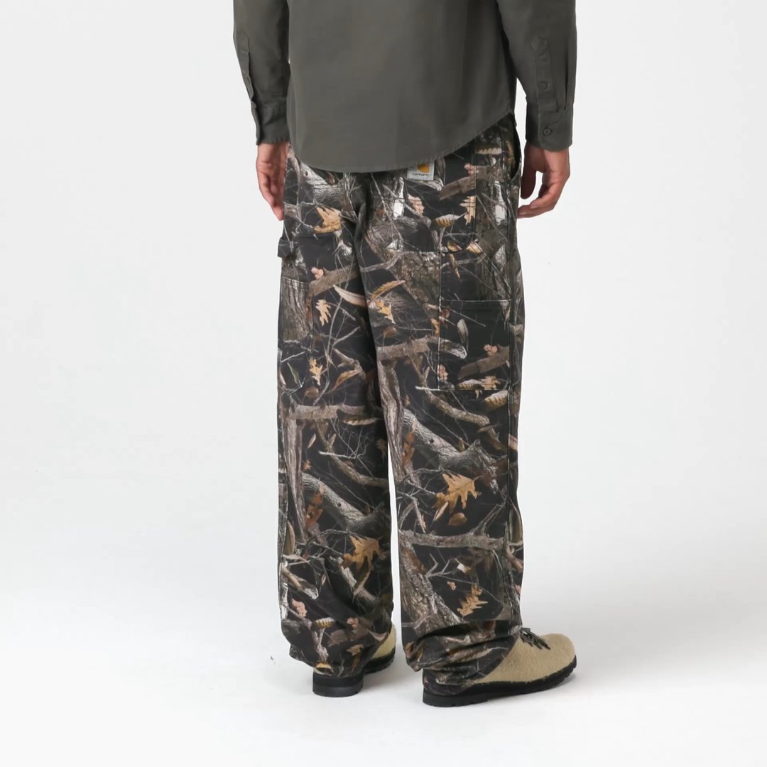 Model wearing a pair of Single Knee Pants in Camo Feather Tree