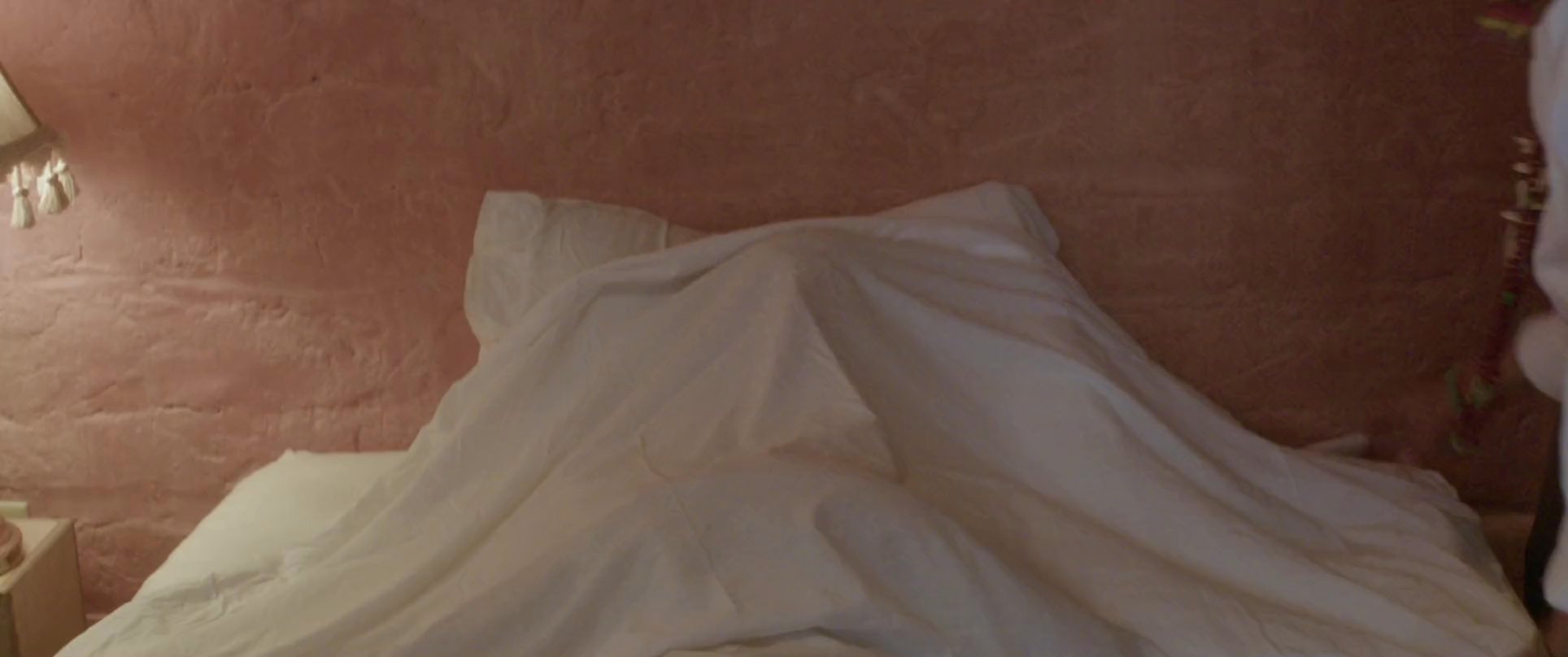 A caregiver tucks a sleeping man into bed before the scene transitions to a tranquil landscape at dusk. The shift from an outdoor orchard to an intimate bedroom highlights a transition from activity to rest.