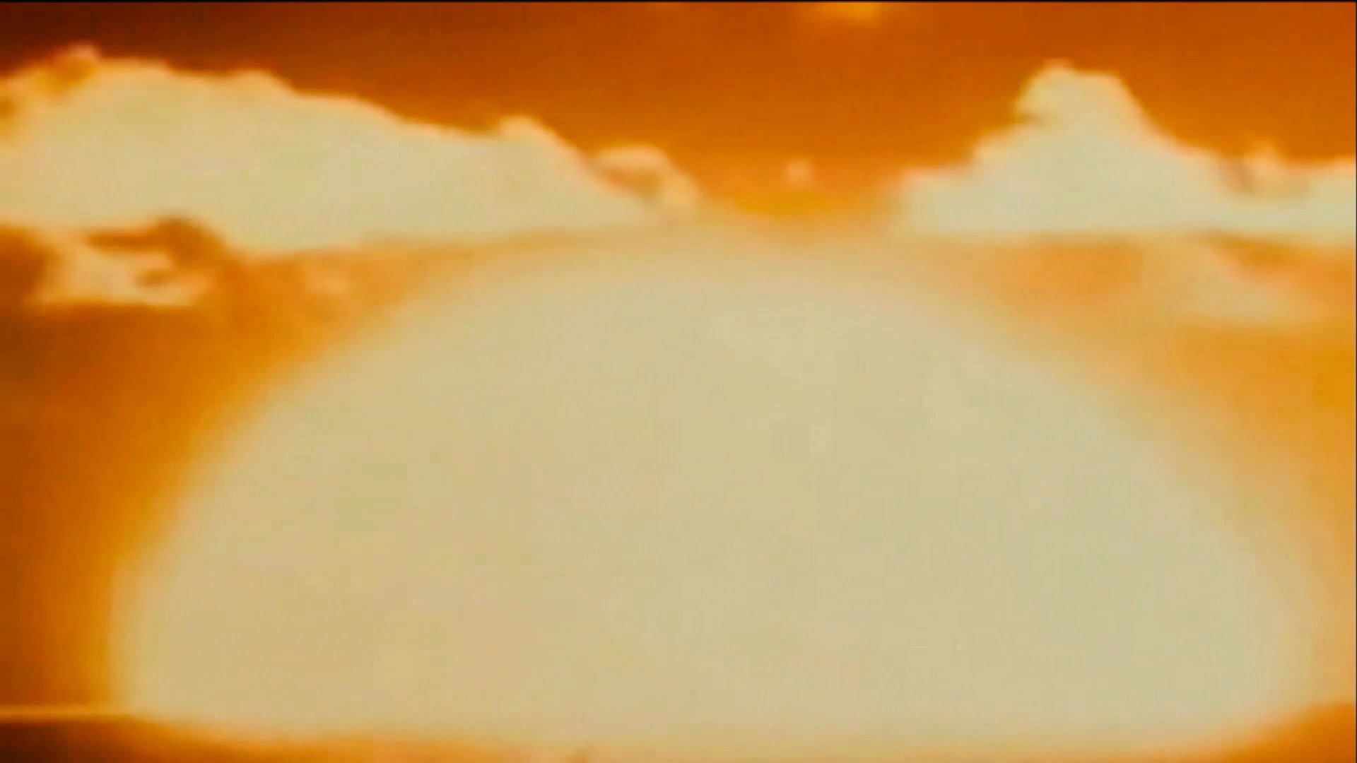 Historical archival footage depicts a series of nuclear test explosions across various landscapes, demonstrating the magnitude of the blasts and their immediate environmental impact.