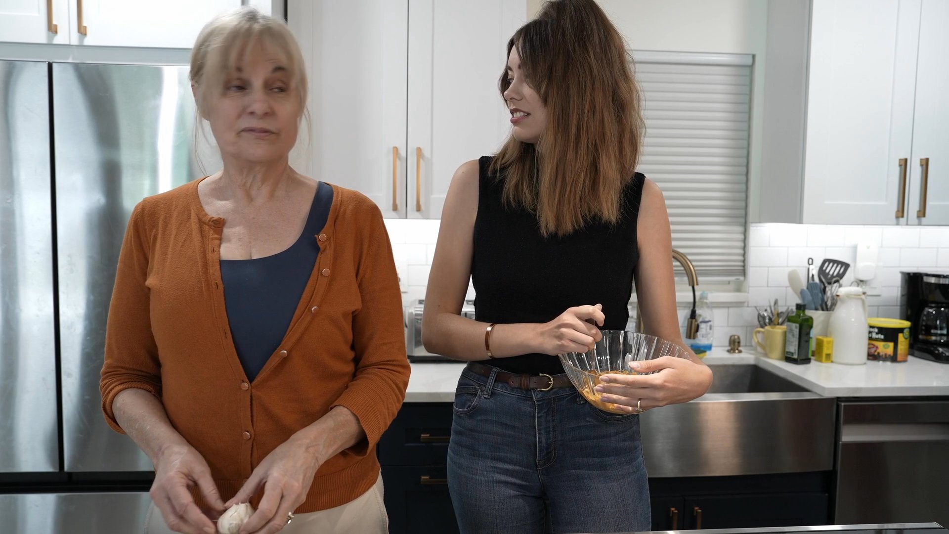 Three women collaborate in a kitchen to prepare a meal, transitioning from group tasks to a social setting before finishing with the oven process.