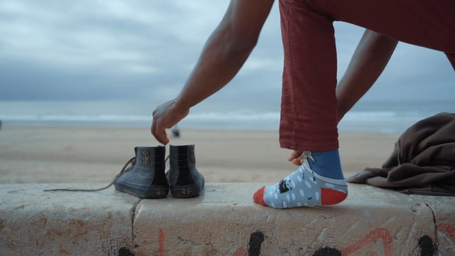 A man emptying the sand from his shoes so he can put them on