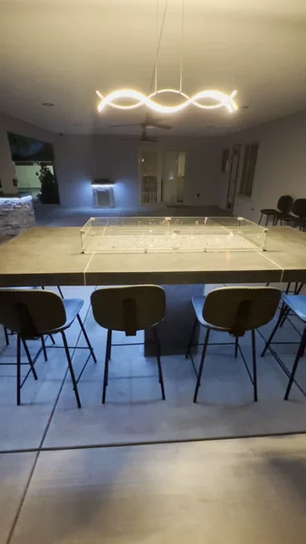 Concrete fire pit table with modern pendant light, fire glass, glass wind guard & bar seating