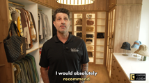 John Werhas standing in his finished walk-in closet with warm wood cabinetry, illuminated display shelves holding handbags, and an island with hat displays, from his Coffee in the Closet testimonial video