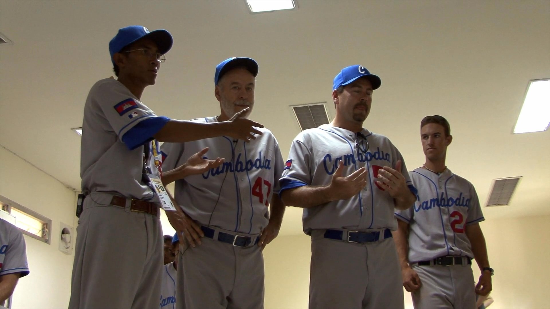 Coaches and players of the Cambodia national baseball team gather in a locker room to discuss strategy and coordinate before a game.