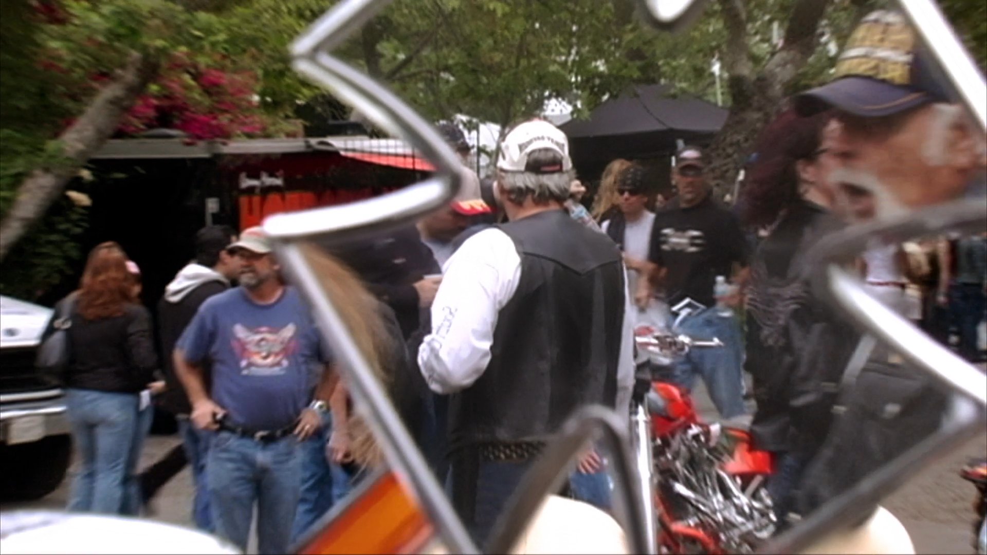 An experienced motorcyclist maneuvers through a scenic route before joining a gathering of riders at an outdoor motorcycle event. Attendees congregate among rows of cruiser bikes, showcasing the camaraderie and scale of the assembly.