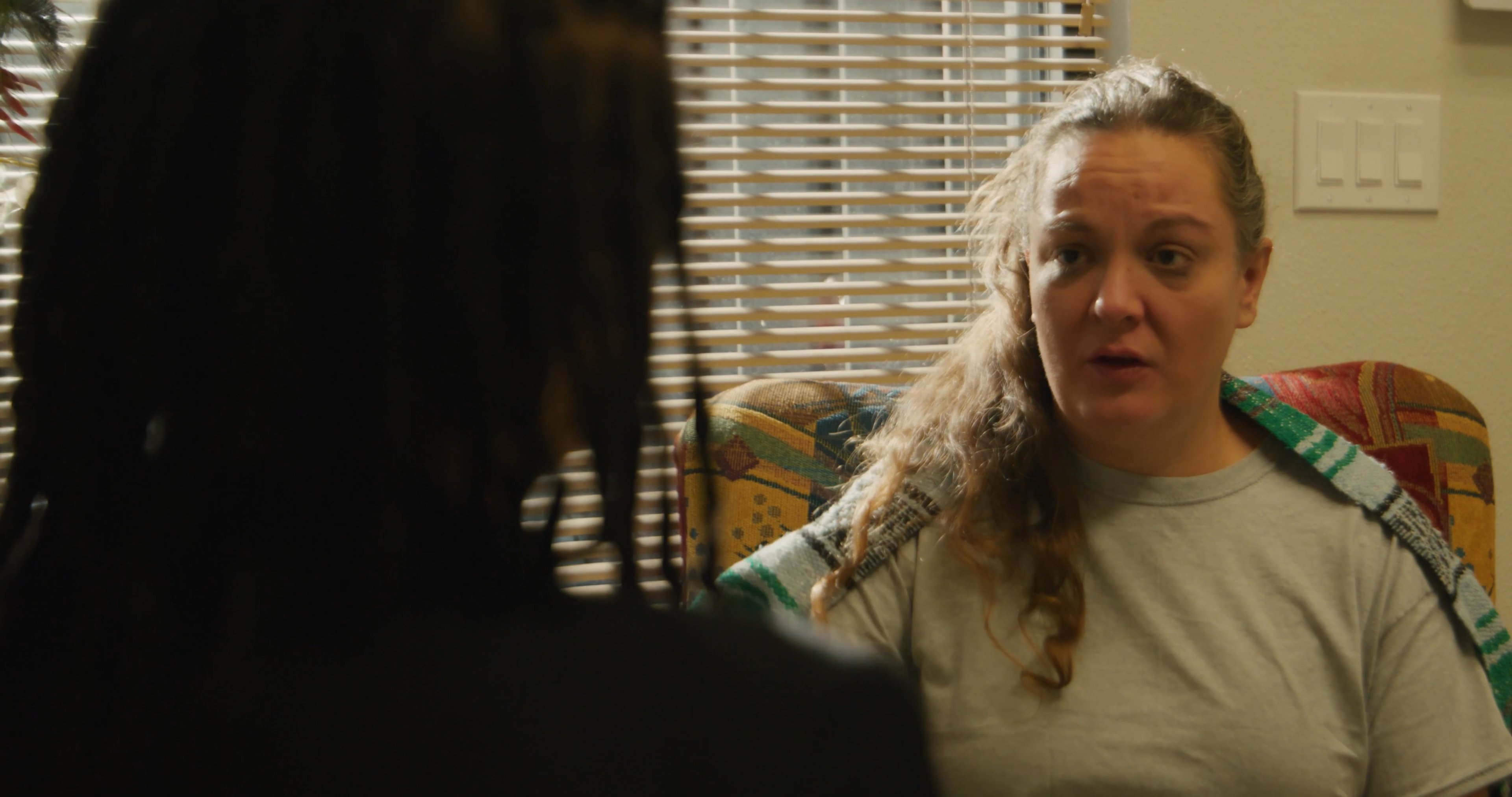 A professional counselor conducts a supportive one-on-one session with a client in a comfortable living room environment. The two engage in a focused, empathetic dialogue to discuss personal wellness and support.