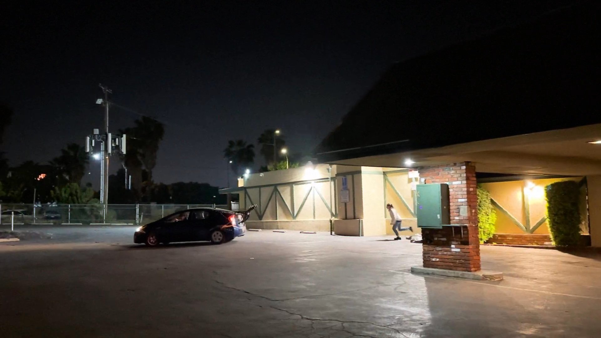 Two individuals conduct surveillance from a parked vehicle at night while a woman walks through a nearby parking lot. The tension escalates as the observers monitor the scene from their car before following the subject.