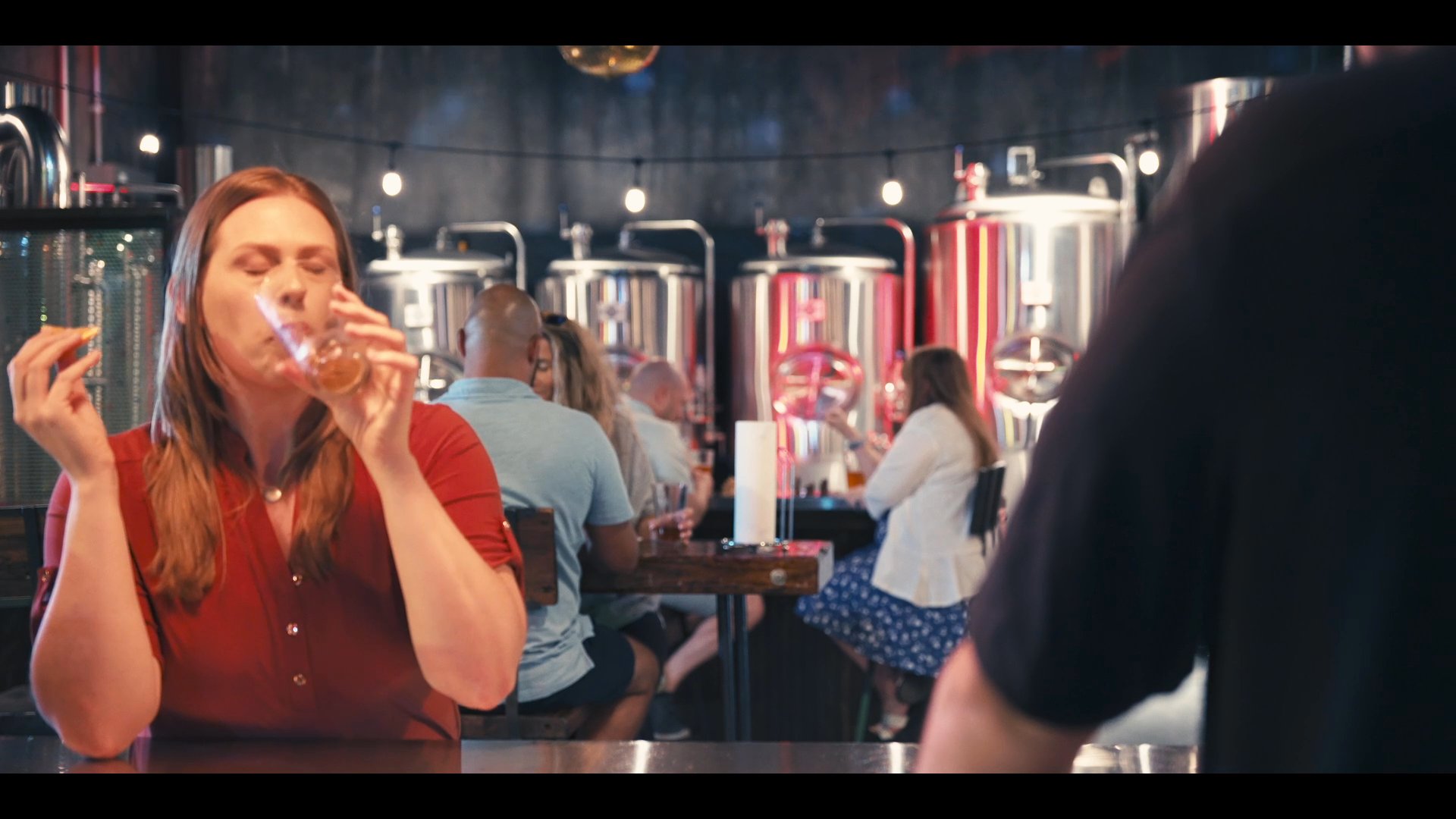 A patron evaluates a beverage at a brewery while receiving service from a staff member. The sequence highlights the professional interaction and product sampling environment.